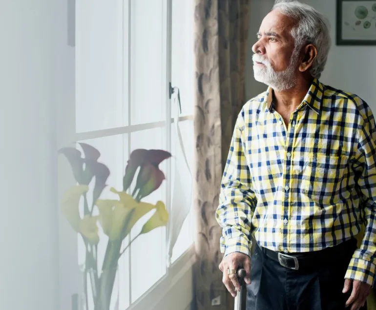 Elderly-Indian-man-with-a-walking-stick-gazing-out-the-window,-symbolising-the-impact-of-chronic-disease-related-muscle-loss