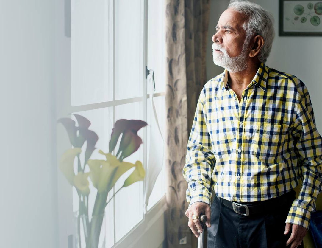 Elderly-Indian-man-with-a-walking-stick-gazing-out-the-window,-symbolising-the-impact-of-chronic-disease-related-muscle-loss