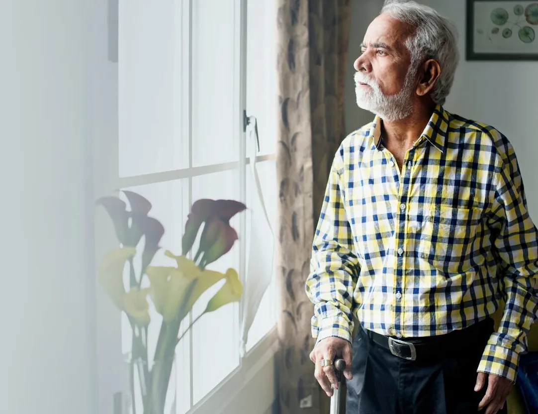Elderly-Indian-man-with-a-walking-stick-gazing-out-the-window,-symbolising-the-impact-of-chronic-disease-related-muscle-loss